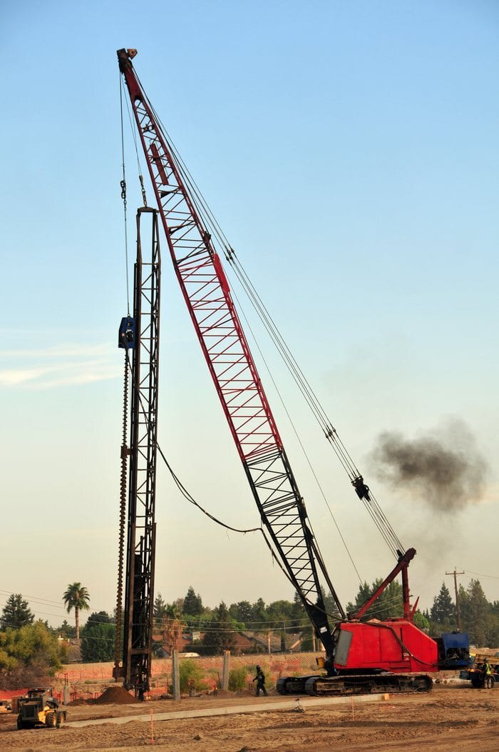 Red lattice boom crawler crane on tracks at a construction site under a blue sky